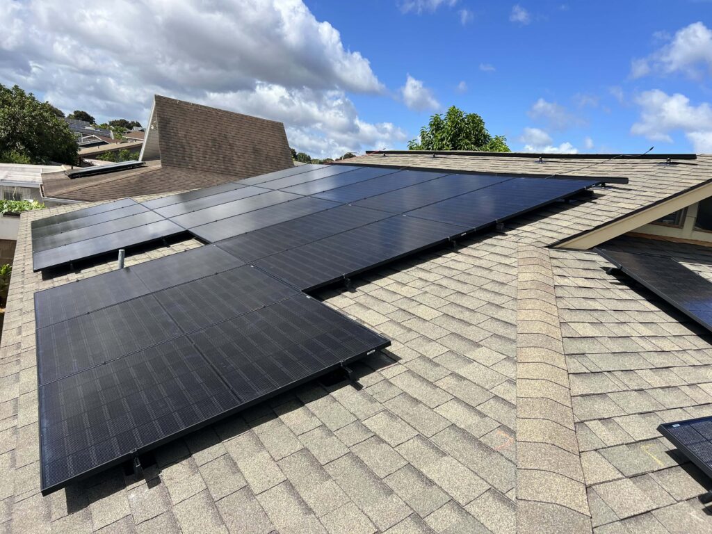 Finished black solar panel installation on a shingle roof against a clear Oʻahu sky